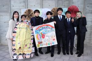 フォトブースの前でタイムカプセルの品とともに記念撮影をする７人の参加者